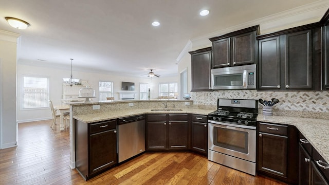 kitchen with a peninsula, light wood-style flooring, a sink, stainless steel appliances, and tasteful backsplash