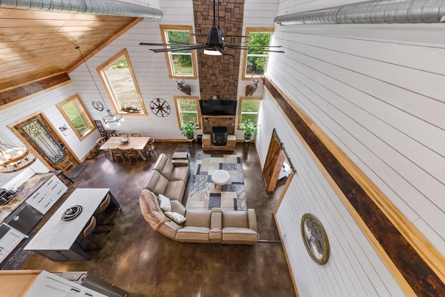 living room with wooden walls, a fireplace, a ceiling fan, and a towering ceiling