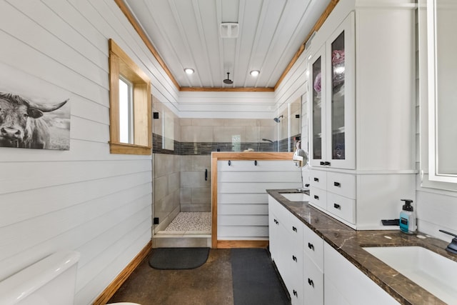 bathroom featuring wooden walls, toilet, double vanity, a stall shower, and a sink