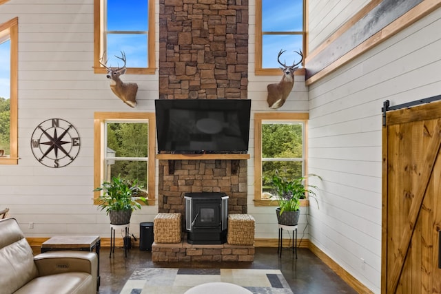 living room with a barn door, concrete floors, wood walls, a towering ceiling, and a wood stove