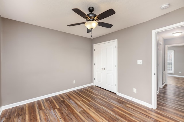 unfurnished bedroom with baseboards, dark wood-style floors, and a ceiling fan