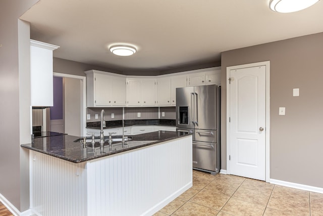 kitchen with dark stone countertops, a peninsula, light tile patterned flooring, high end fridge, and a sink