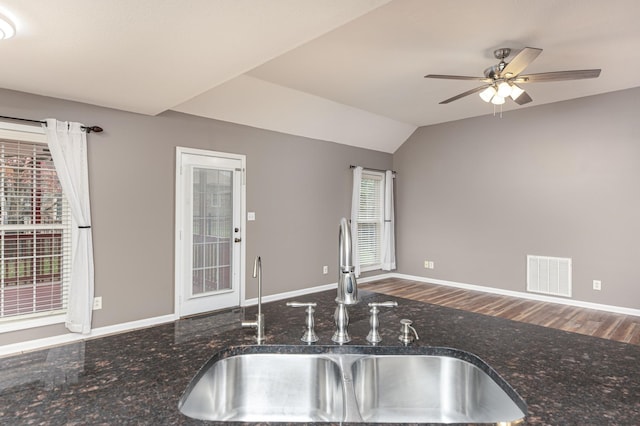 kitchen featuring visible vents, a sink, dark stone counters, lofted ceiling, and ceiling fan