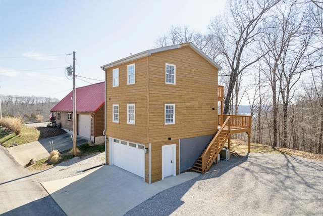 view of side of home with stairs, an attached garage, cooling unit, and gravel driveway