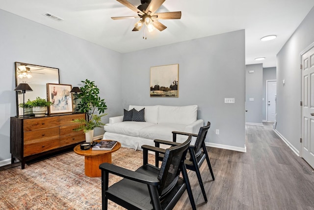 living area featuring visible vents, baseboards, dark wood finished floors, and a ceiling fan