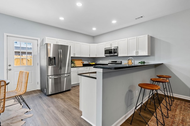 kitchen featuring visible vents, a kitchen bar, dark countertops, appliances with stainless steel finishes, and a peninsula