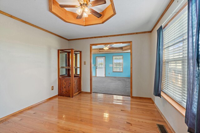 spare room with visible vents, crown molding, baseboards, light wood-type flooring, and a tray ceiling