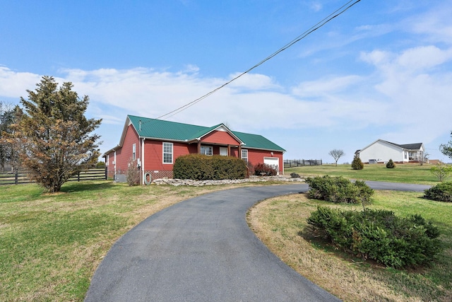 ranch-style house featuring a front yard, fence, driveway, a garage, and metal roof