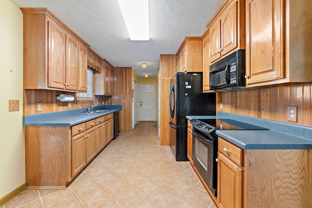 kitchen with light tile patterned floors, a sink, black appliances, wood walls, and a textured ceiling