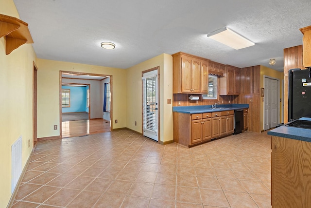 kitchen with a sink, a textured ceiling, black appliances, and light tile patterned floors