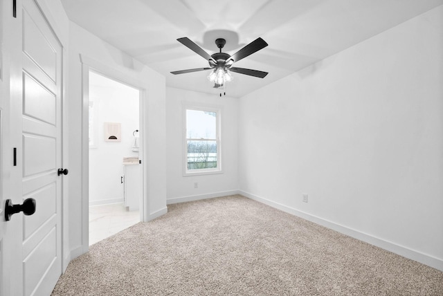 unfurnished bedroom featuring light colored carpet, connected bathroom, baseboards, and a ceiling fan