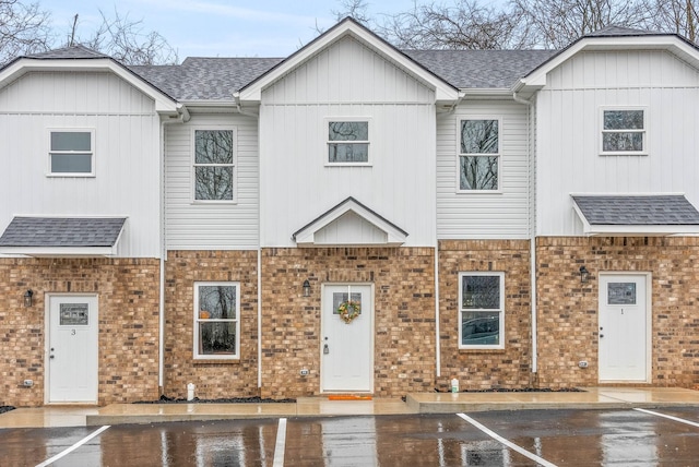 view of property with brick siding, uncovered parking, and a shingled roof