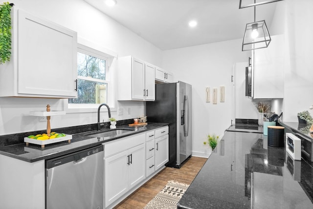 kitchen with wood finished floors, dark stone counters, a sink, stainless steel appliances, and white cabinets