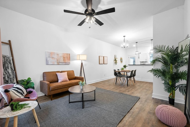 living area featuring ceiling fan with notable chandelier, baseboards, and wood finished floors