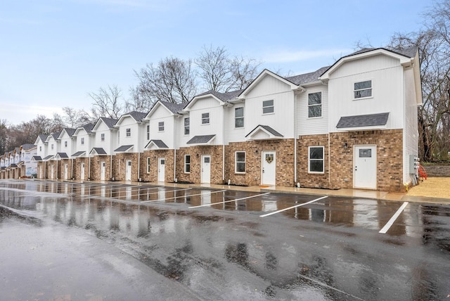 view of front of property featuring roof with shingles, brick siding, uncovered parking, a residential view, and board and batten siding