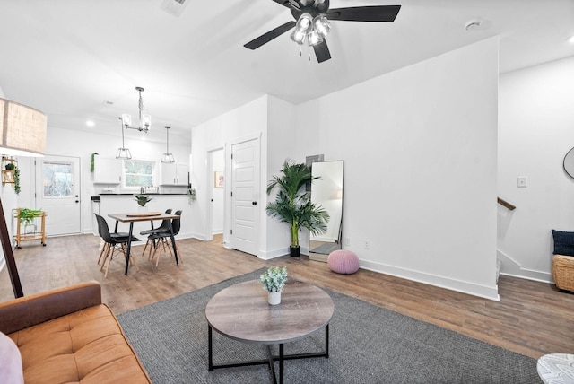 living area with ceiling fan with notable chandelier, recessed lighting, wood finished floors, and baseboards