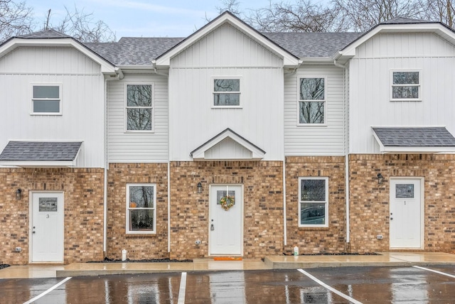 view of property featuring brick siding, a shingled roof, and uncovered parking