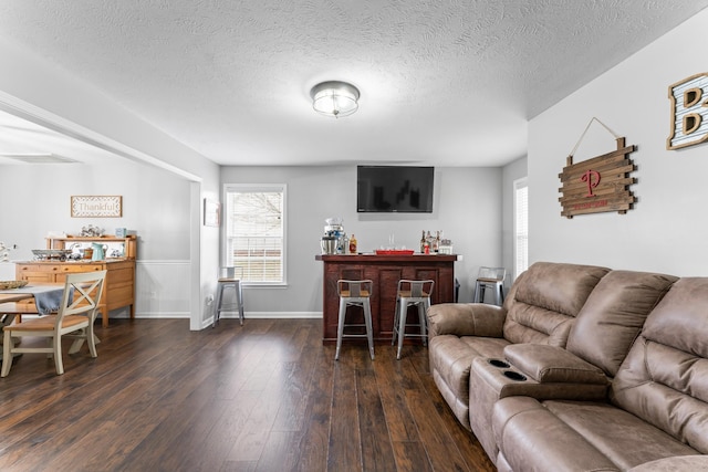 living room with visible vents, a textured ceiling, dark wood-style floors, a bar, and baseboards