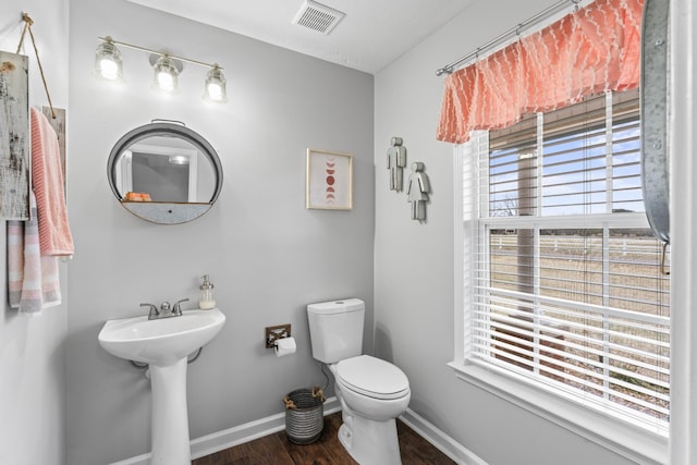 half bath featuring wood finished floors, baseboards, visible vents, a sink, and toilet