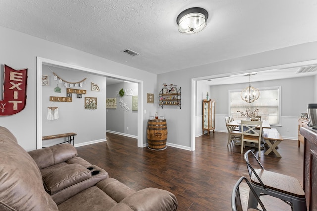 living area featuring an inviting chandelier, dark wood-style floors, visible vents, and a textured ceiling