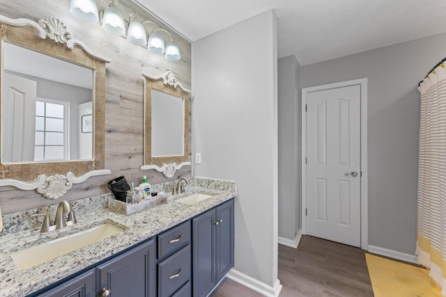 full bath featuring double vanity, wood finished floors, baseboards, and a sink