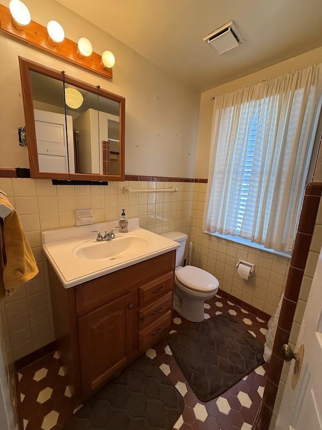 bathroom with vanity, visible vents, wainscoting, tile walls, and toilet