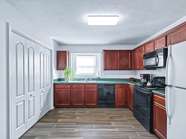 kitchen with black appliances, dark countertops, reddish brown cabinets, and a sink