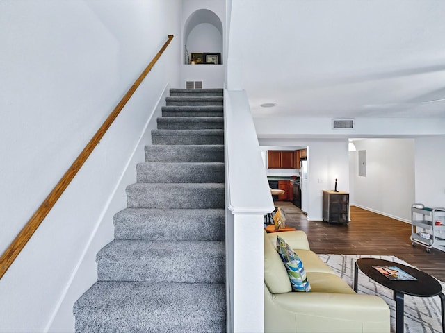 staircase featuring electric panel, visible vents, and wood finished floors