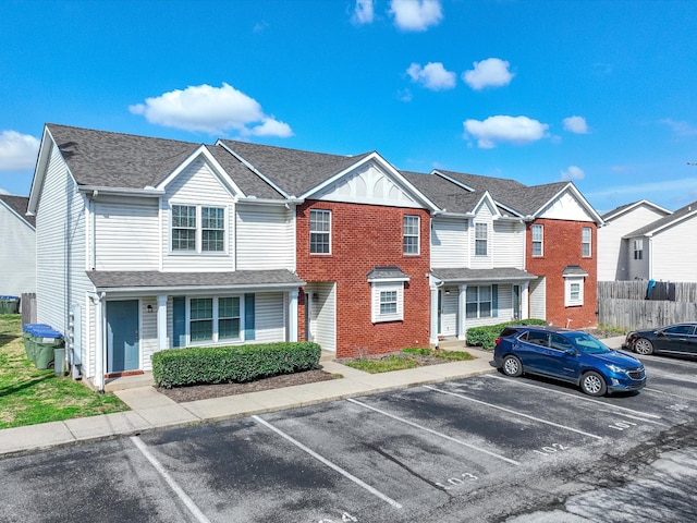 townhome / multi-family property with fence, roof with shingles, uncovered parking, a residential view, and brick siding