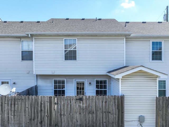 back of property with fence and a shingled roof