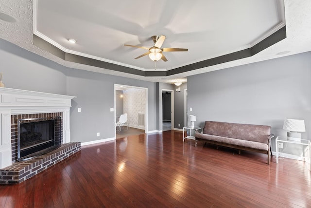 unfurnished room with hardwood / wood-style floors, baseboards, a tray ceiling, a fireplace, and ornamental molding