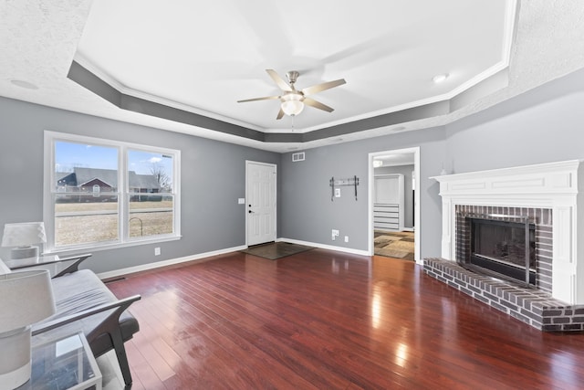 unfurnished living room with baseboards, a raised ceiling, hardwood / wood-style floors, and crown molding