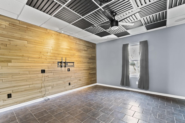 empty room with an accent wall, wooden walls, a ceiling fan, and baseboards