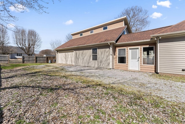 rear view of house with an attached garage, fence, driveway, and roof with shingles