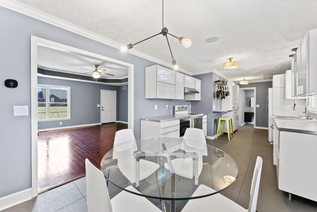 dining area with wood finished floors, baseboards, ceiling fan, ornamental molding, and a textured ceiling