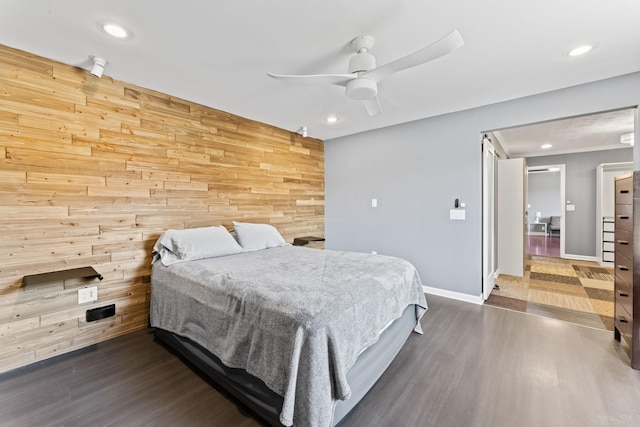 bedroom featuring an accent wall, baseboards, dark wood-style flooring, and wood walls