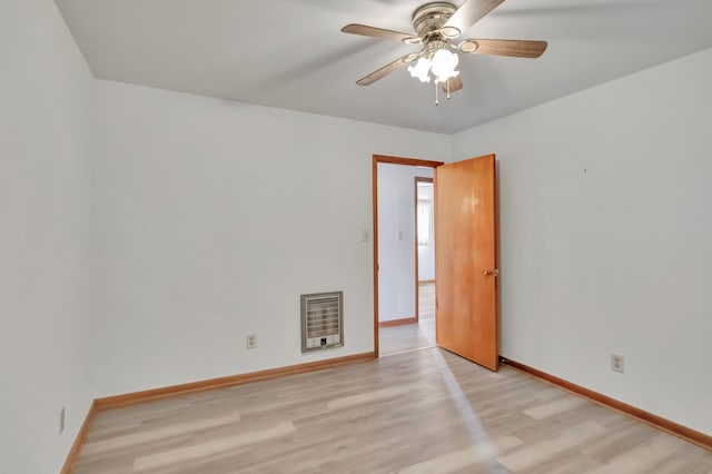 spare room featuring heating unit, baseboards, light wood-type flooring, and ceiling fan