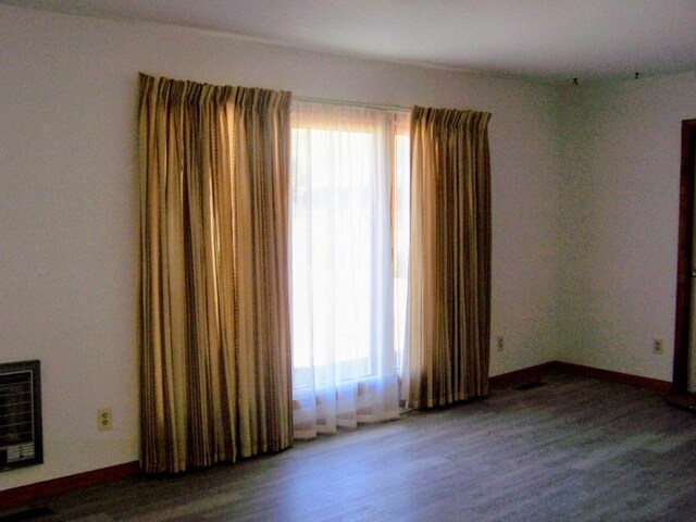 unfurnished room with baseboards, heating unit, and wood finished floors