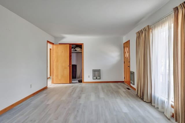 unfurnished room with baseboards, heating unit, and light wood-style floors