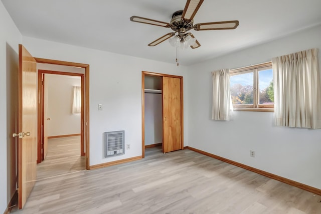 unfurnished bedroom featuring baseboards, heating unit, a closet, and light wood finished floors