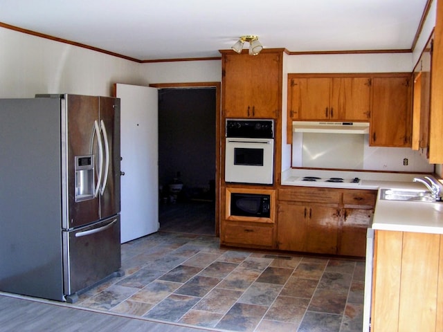 kitchen featuring white appliances, brown cabinetry, a sink, light countertops, and under cabinet range hood