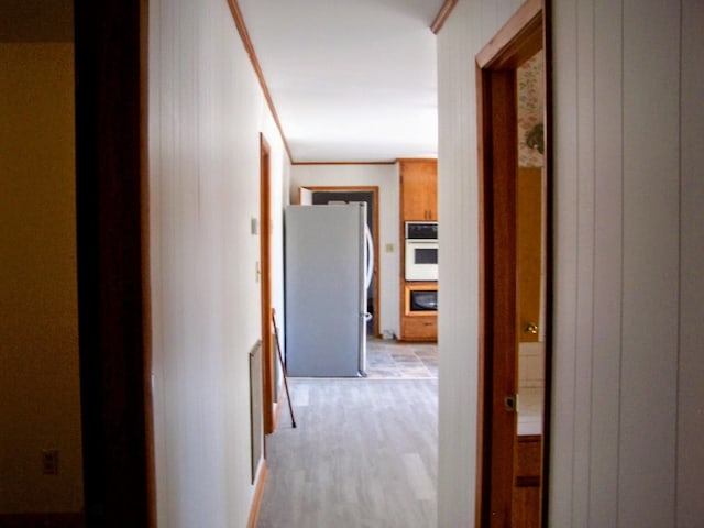 hallway with light wood-style floors, wood walls, and ornamental molding