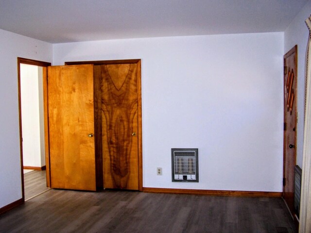 unfurnished bedroom with heating unit, a closet, baseboards, and wood finished floors