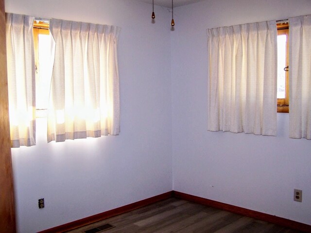 spare room with wood finished floors, visible vents, and baseboards