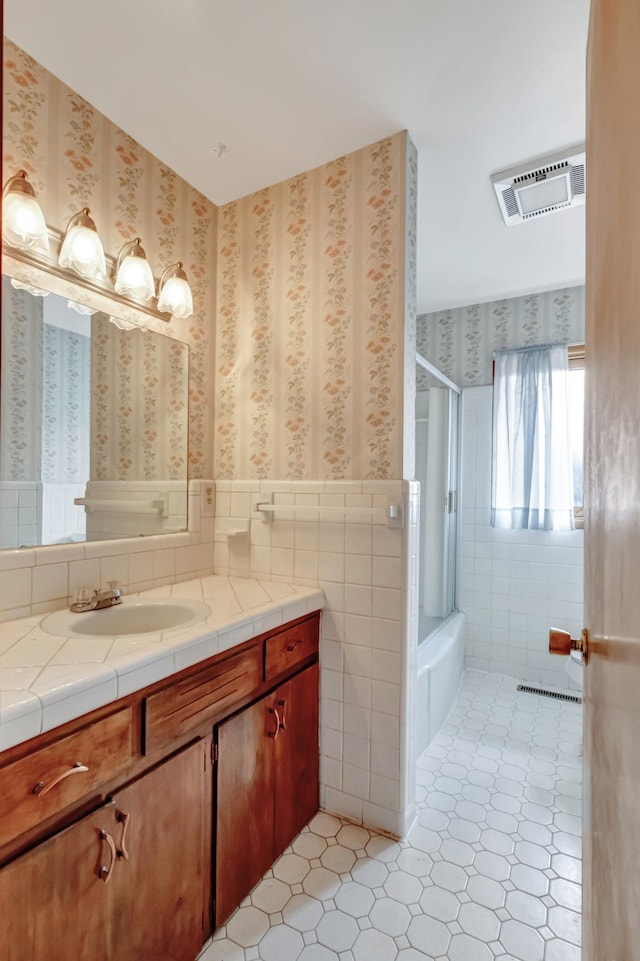 bathroom featuring visible vents, wainscoting, wallpapered walls, and tile walls