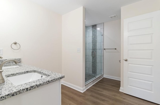 bathroom featuring wood finished floors, baseboards, double vanity, a sink, and a shower stall