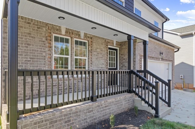 view of exterior entry with a garage, brick siding, and covered porch