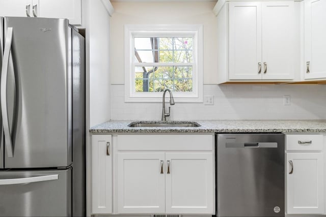 kitchen featuring light stone counters, decorative backsplash, white cabinets, stainless steel appliances, and a sink