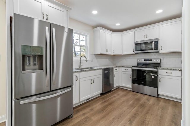 kitchen featuring tasteful backsplash, wood finished floors, white cabinets, stainless steel appliances, and a sink