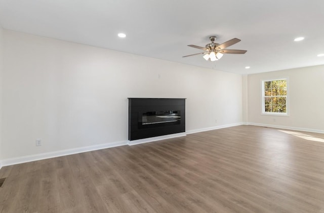 unfurnished living room with baseboards, wood finished floors, and a glass covered fireplace